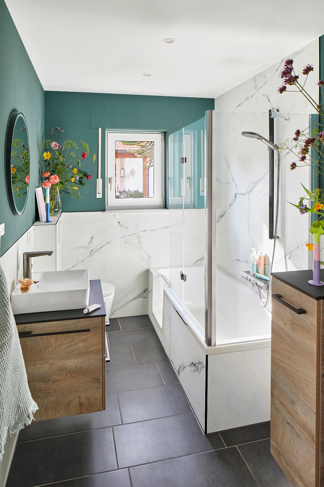 Moderne badkamer met marmerlook tegels, houtlook meubel, groene wand en ligbad met glazen wand.